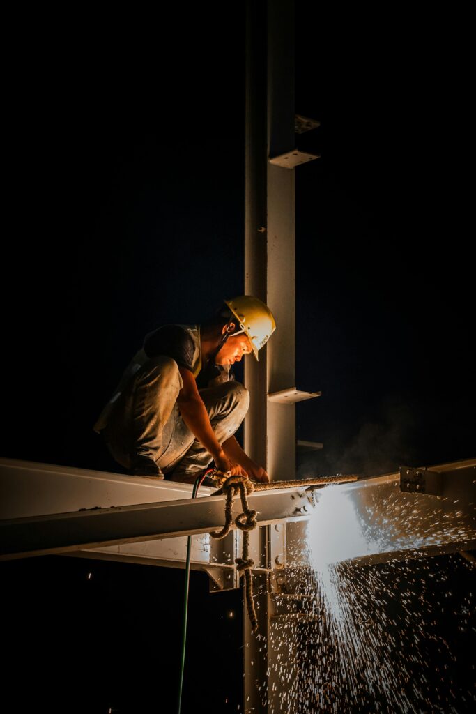 Industrial worker welding steel structure at night, casting bright sparks.