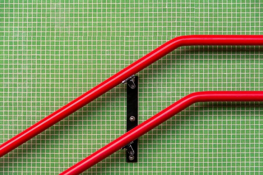 Modern abstract composition of red railings against a green tiled wall, showcasing vibrant contrast.